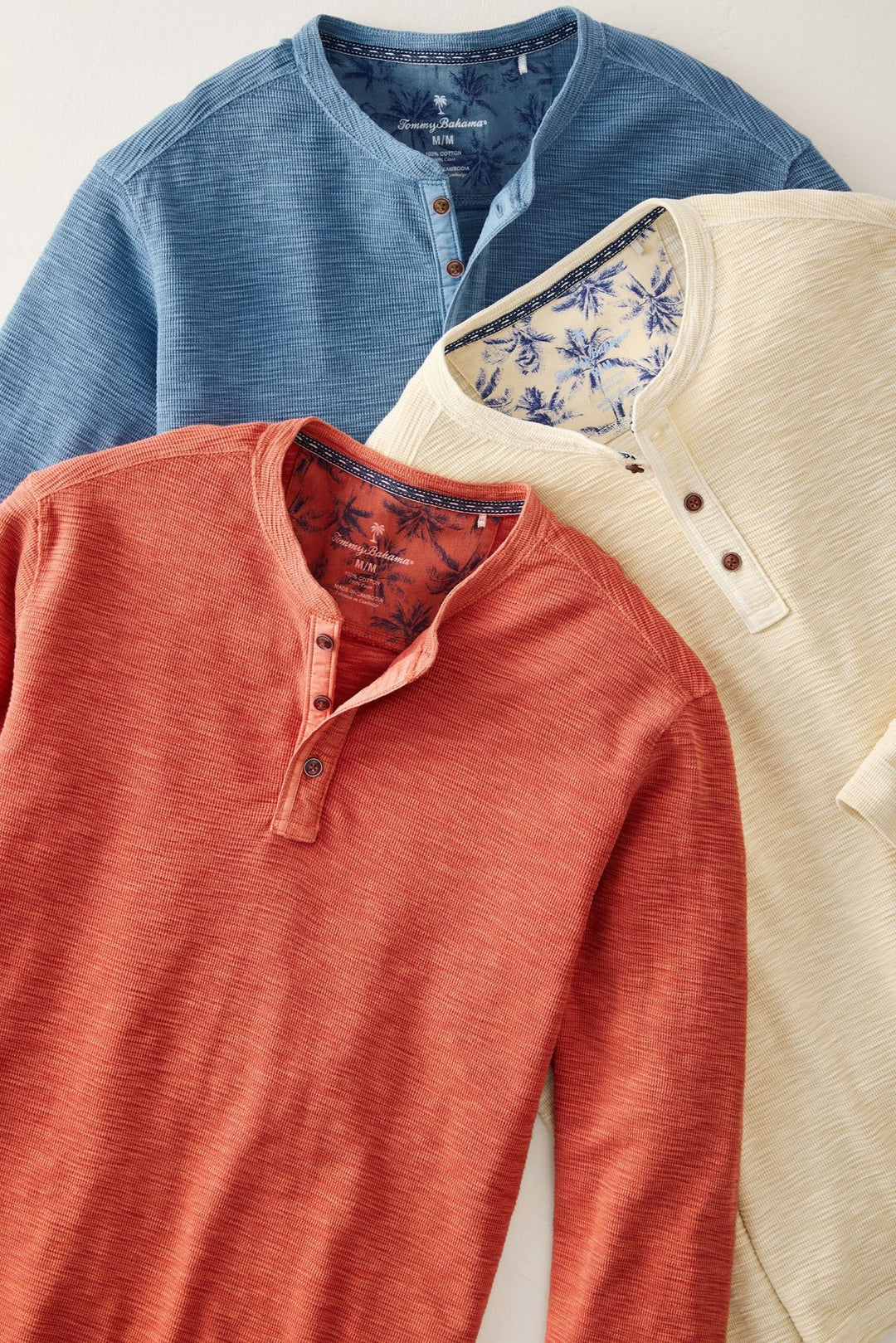 Three long-sleeve henley shirts in blue, red, and beige on a light gray background.