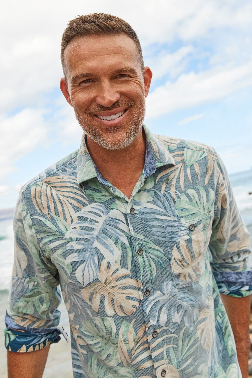 Man wearing a Tommy Bahama tropical patterned shirt with a beach background
