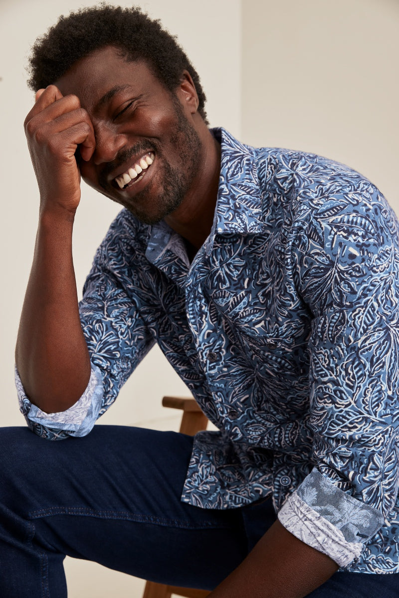 Man wearing a blue patterned shirt sitting on a chair with a neutral background