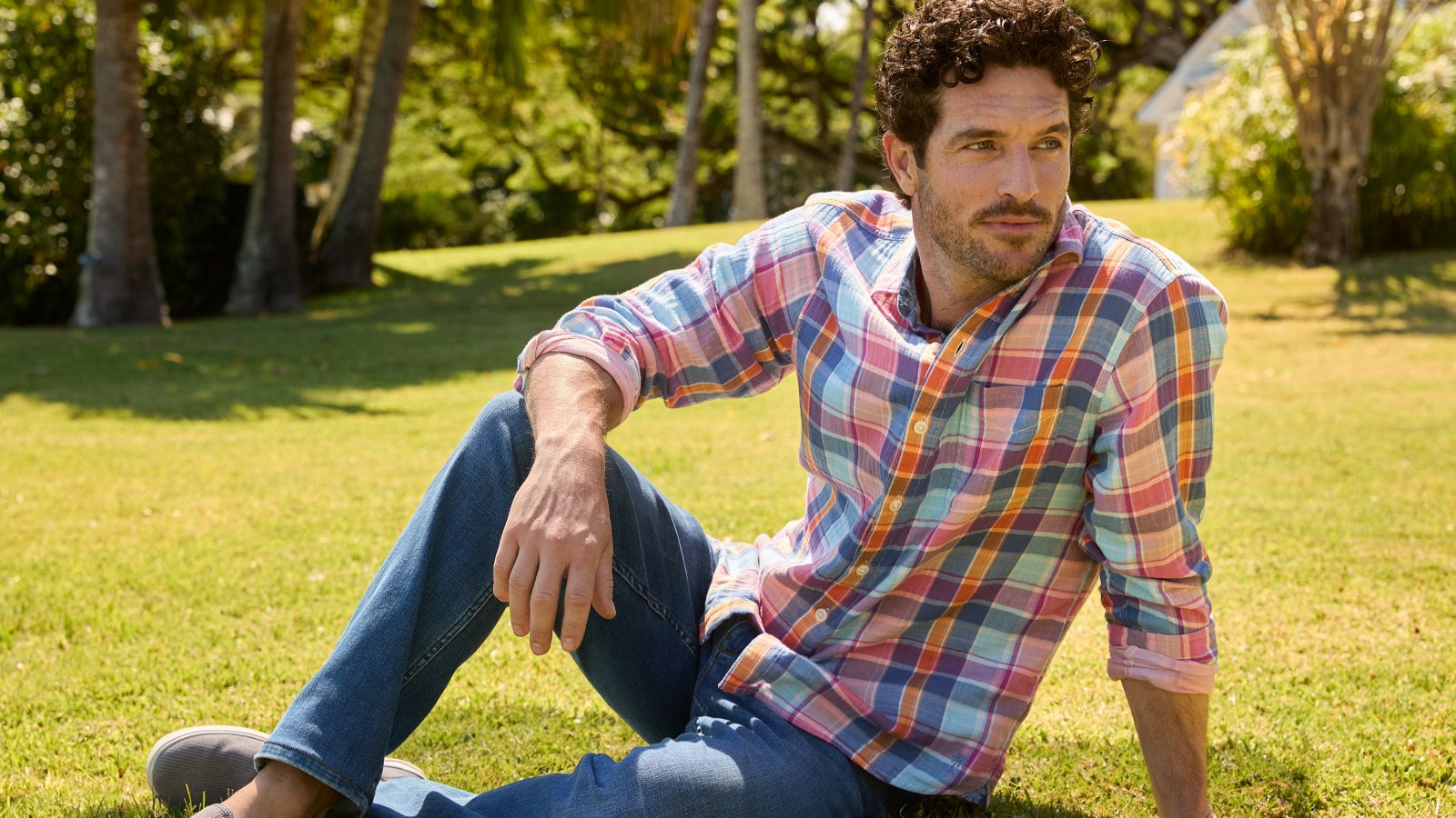 Man sitting on grass wearing a plaid shirt and jeans
