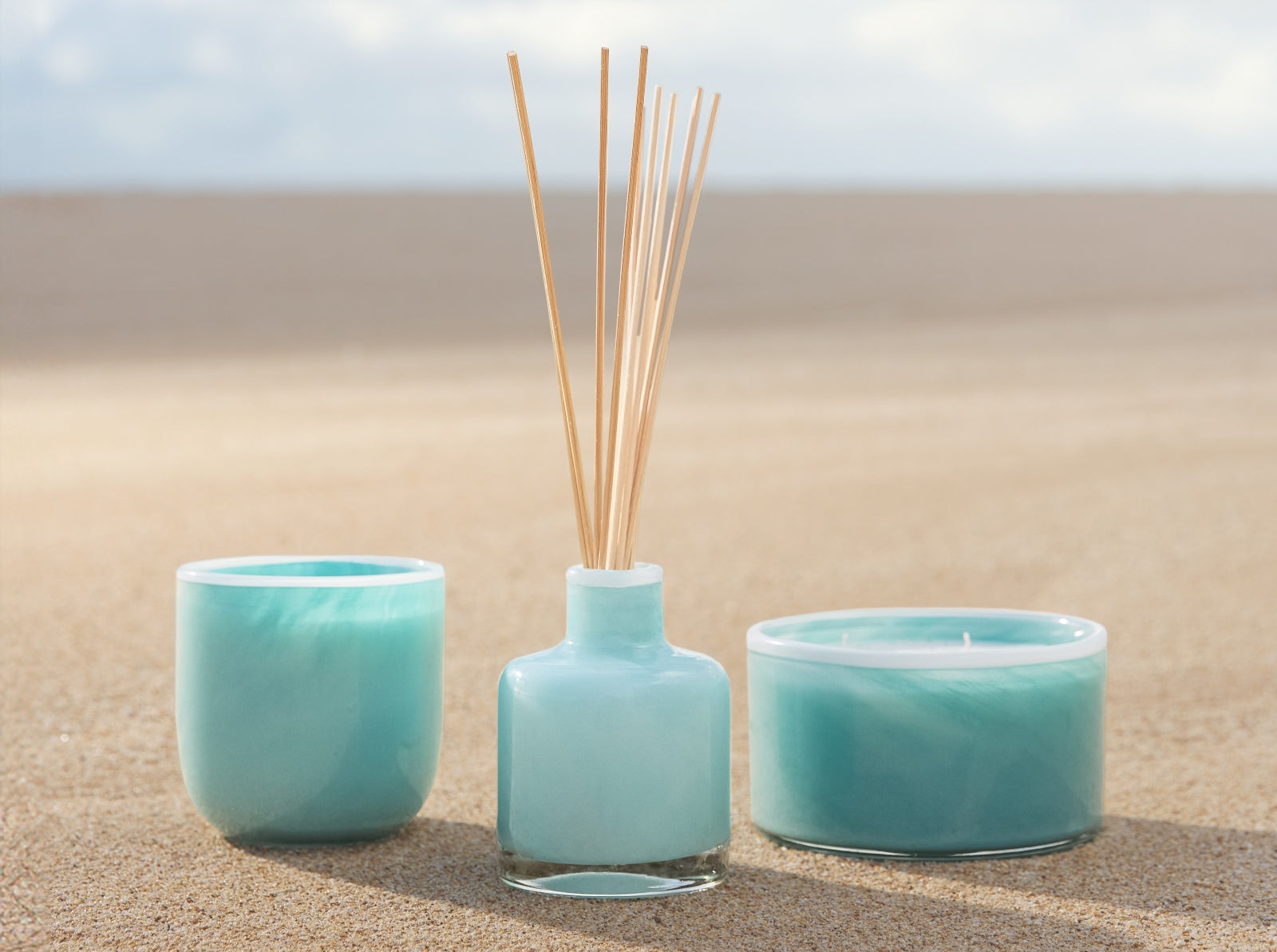 Three turquoise ceramic items on a sandy surface with a blurred natural background