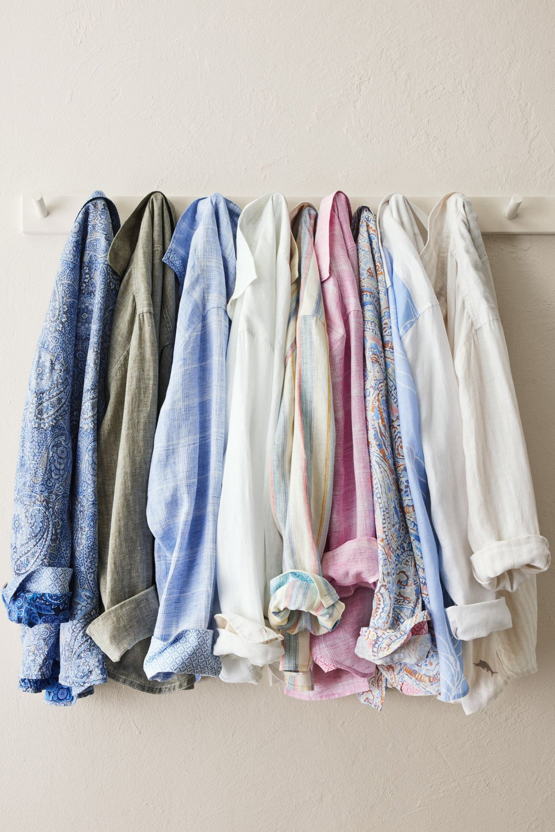 Collection of colorful shirts hanging on a rack against a white wall