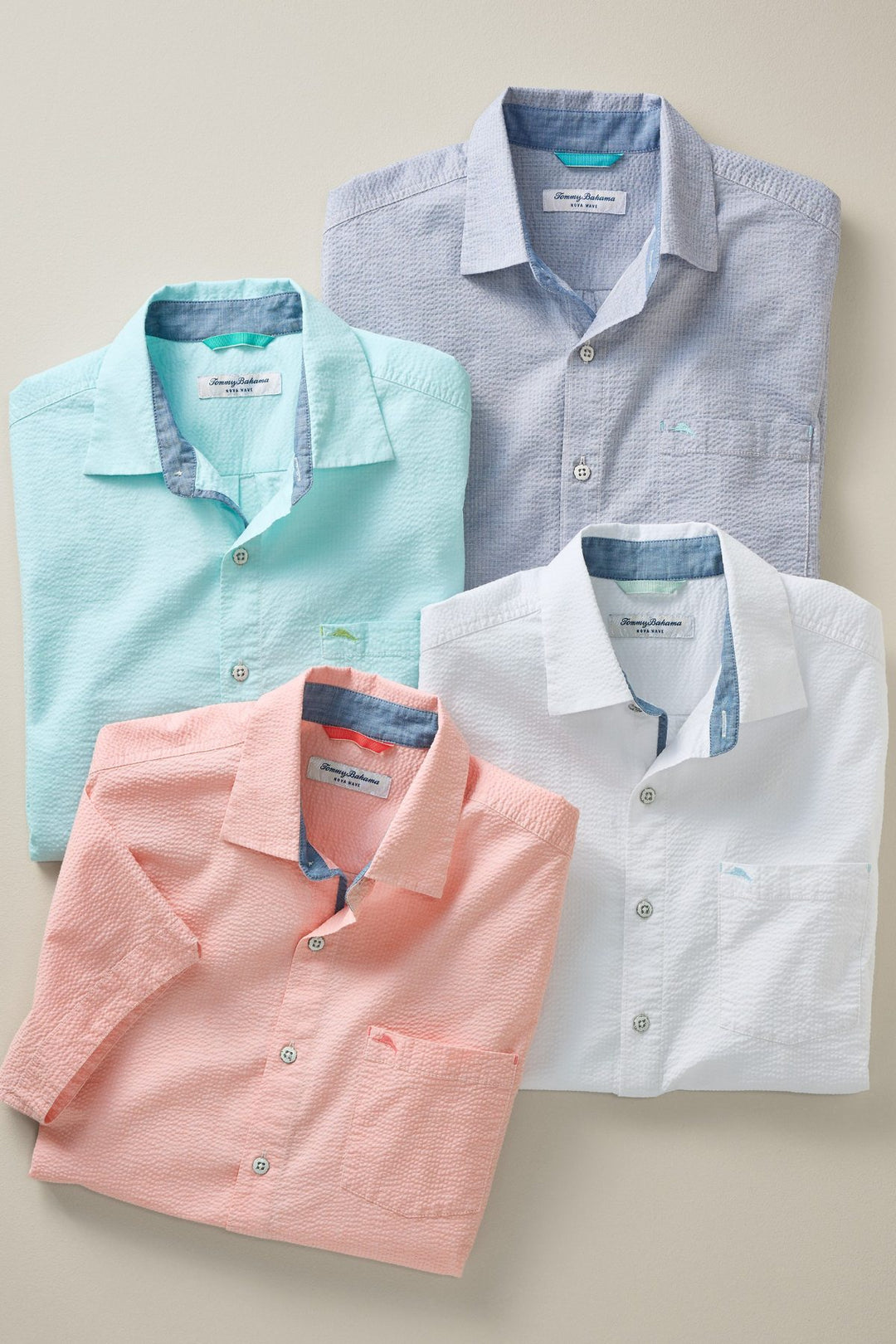 Four folded dress shirts in different colors on a beige background