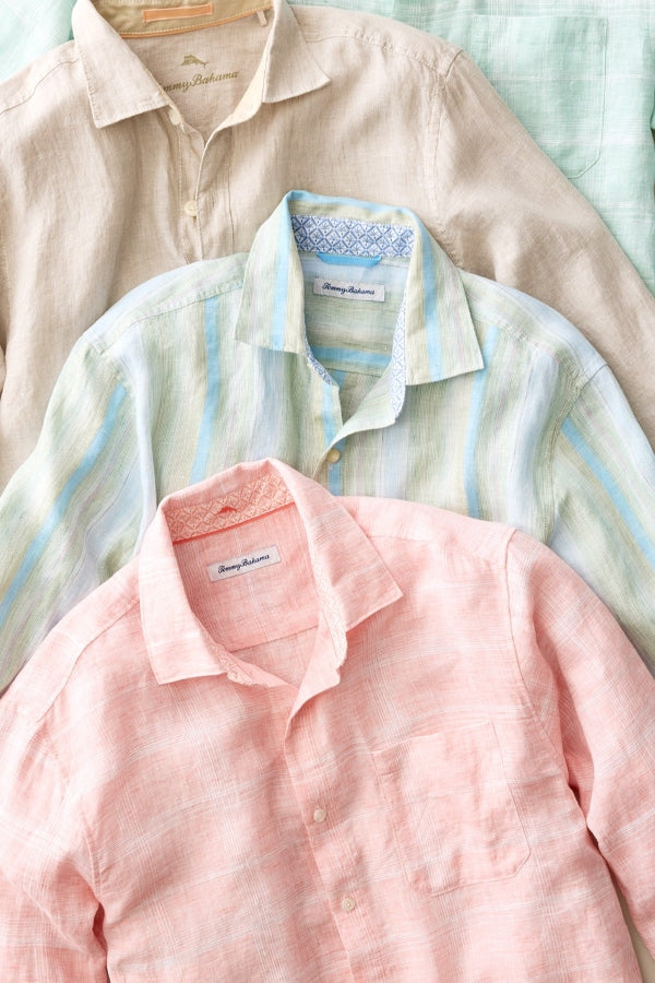 Three men's long-sleeve linen button-down shirts in peach, light blue and white striped, and beige, arranged overlapping on a textured fabric background.